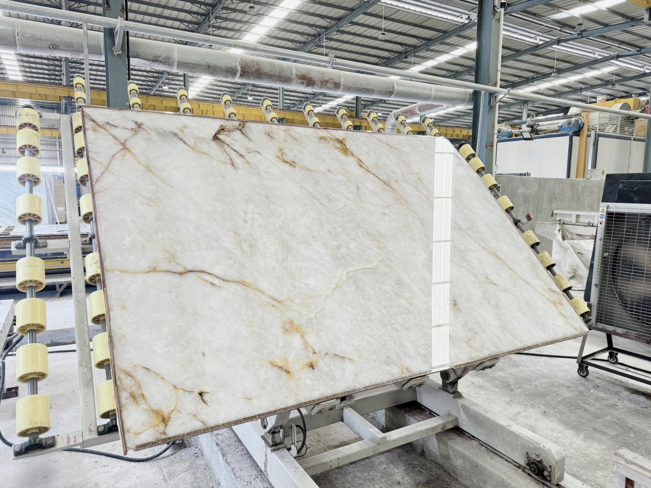 Polished Cristallo Quartzite slab with a crystalline white background and natural gold-brown veining during factory processing Polished Cristallo Quartzite slab with a crystalline white background and natural gold-brown veining during factory processing